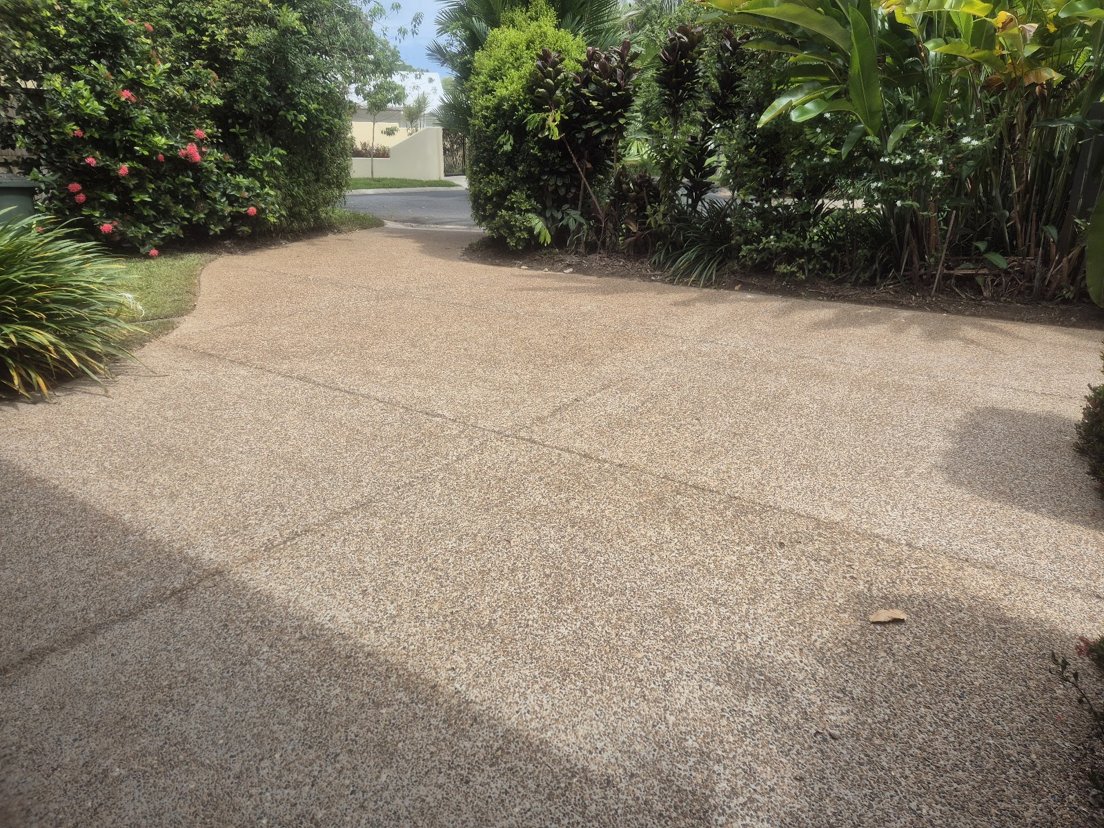 A freshly cleaned exposed aggregate driveway edged by tropical garden