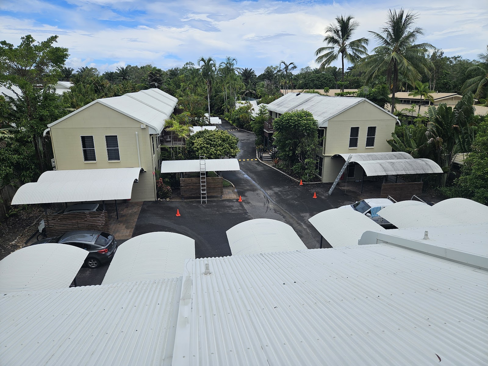 White roofs across a Port Douglas unit complex during a roof clean, ladder and safety cones set up below