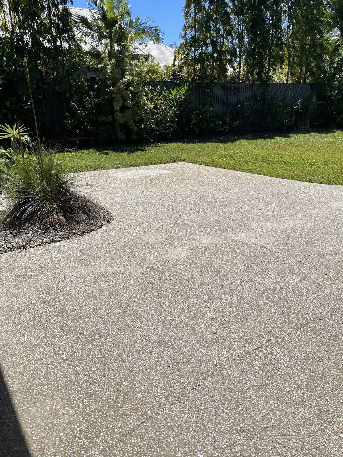 A clean concrete patio beside a lawn and garden hedge