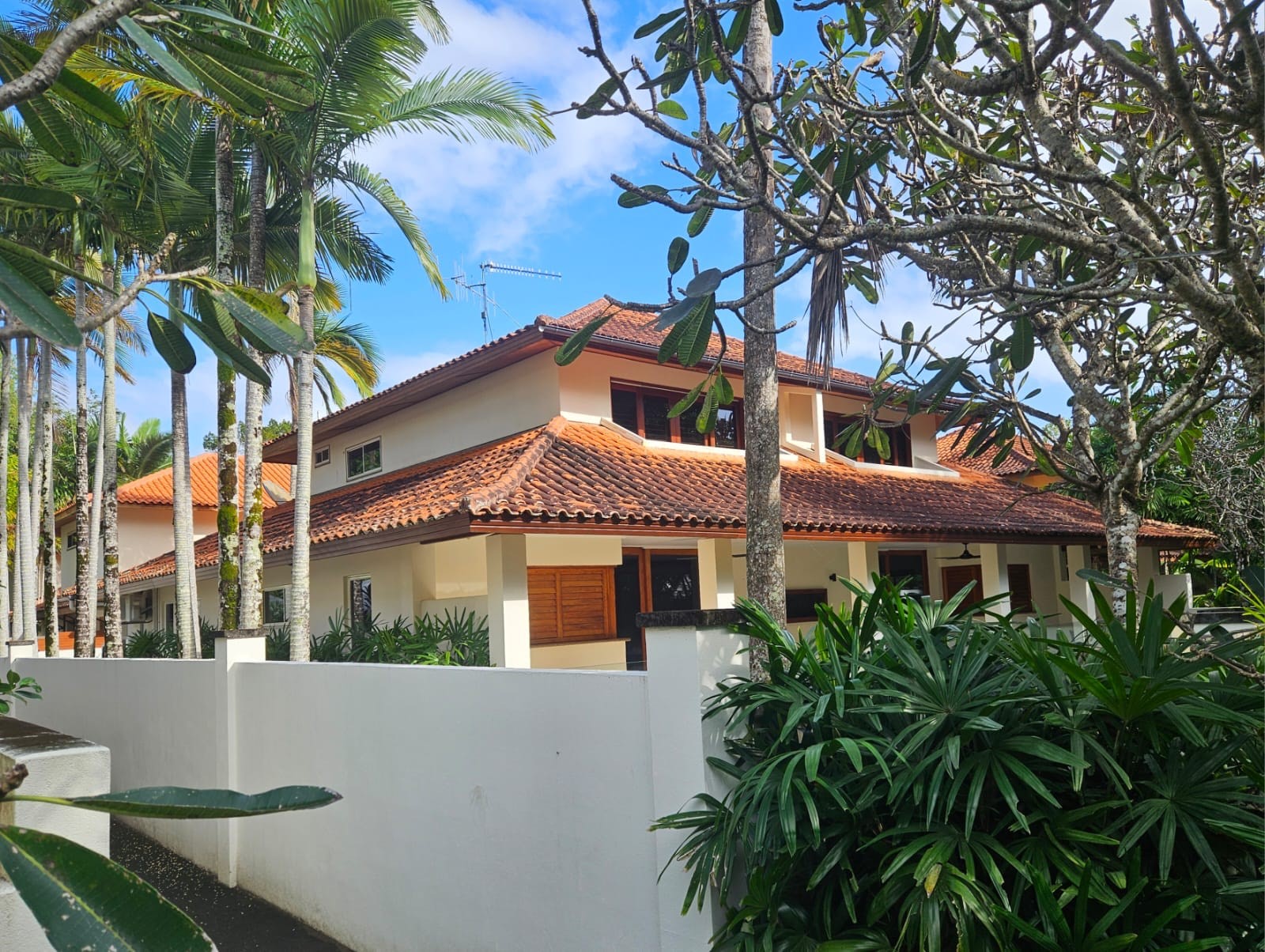 A two storey Port Douglas villa with a terracotta roof and freshly cleaned white boundary wall